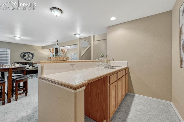 kitchen with sink, hanging light fixtures, tile counters, light colored carpet, and kitchen peninsula