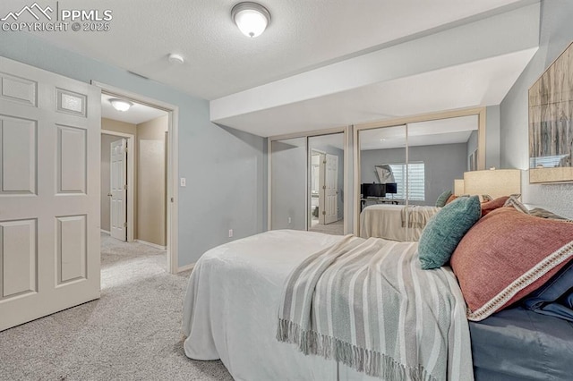 bedroom with a textured ceiling, light carpet, and two closets