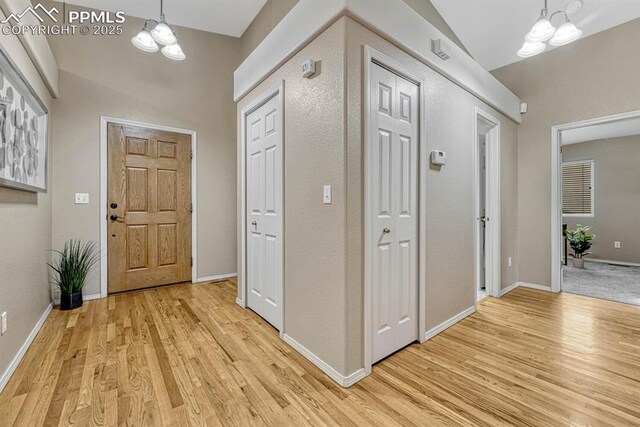 entrance foyer featuring a chandelier, vaulted ceiling, and light wood-type flooring