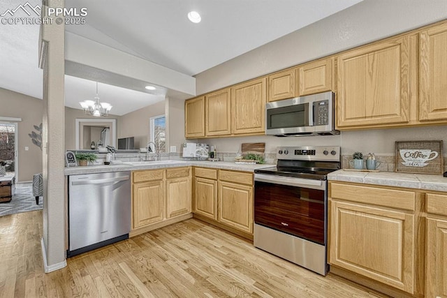 kitchen with light brown cabinets, stainless steel appliances, lofted ceiling, and a notable chandelier