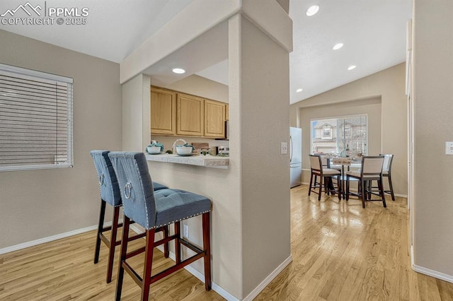 kitchen with light brown cabinets, white refrigerator, light hardwood / wood-style flooring, a breakfast bar area, and lofted ceiling