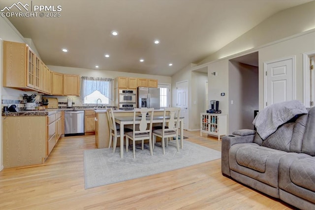 kitchen featuring a center island, stainless steel appliances, light stone counters, lofted ceiling, and light wood-type flooring