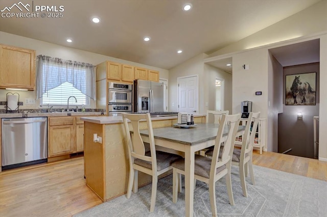 kitchen with light brown cabinetry, stainless steel appliances, light hardwood / wood-style flooring, a kitchen island, and lofted ceiling