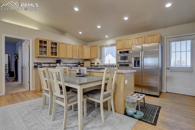 kitchen with light brown cabinets, lofted ceiling, light hardwood / wood-style flooring, appliances with stainless steel finishes, and a kitchen island