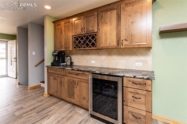 kitchen featuring dark stone countertops, tasteful backsplash, beverage cooler, and light hardwood / wood-style flooring