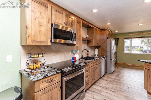 kitchen featuring appliances with stainless steel finishes, tasteful backsplash, sink, light hardwood / wood-style flooring, and dark stone countertops