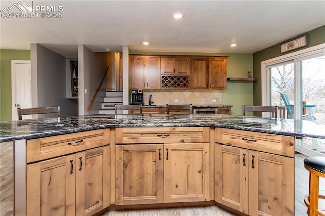 kitchen with a breakfast bar, dark stone countertops, backsplash, and light hardwood / wood-style flooring