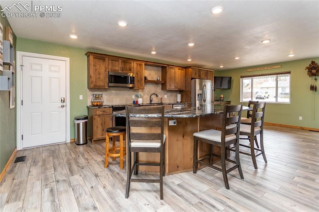 kitchen with a kitchen bar, sink, light wood-type flooring, and appliances with stainless steel finishes