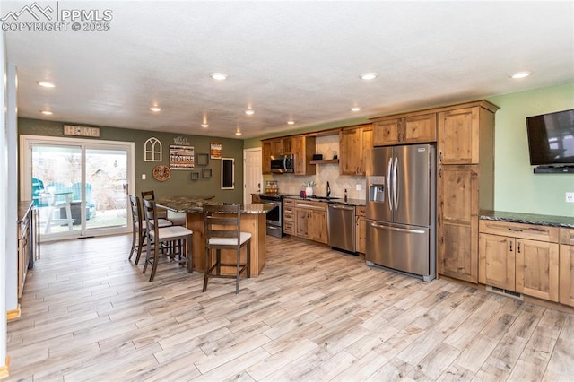 kitchen with dark stone countertops, light hardwood / wood-style floors, a breakfast bar area, a kitchen island, and appliances with stainless steel finishes