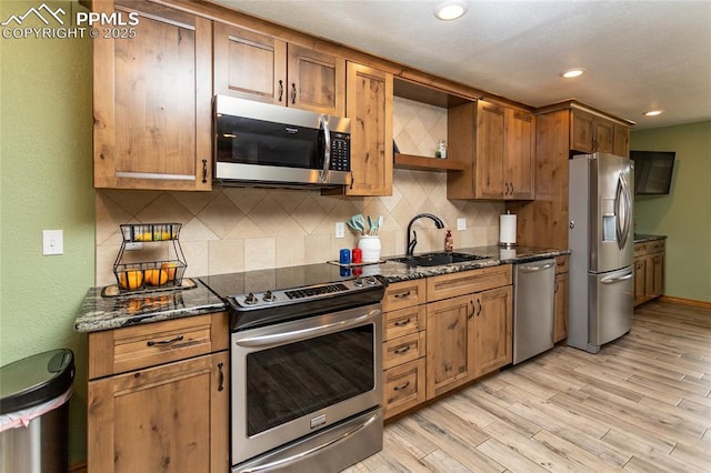 kitchen featuring backsplash, dark stone counters, sink, appliances with stainless steel finishes, and light hardwood / wood-style floors