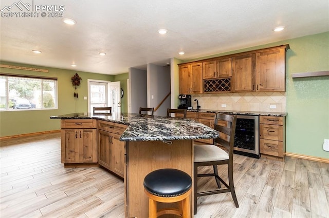 kitchen with a breakfast bar, a center island, beverage cooler, and dark stone counters