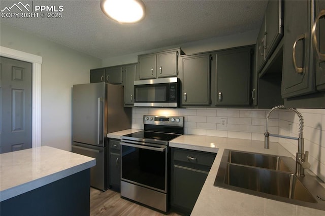 kitchen featuring appliances with stainless steel finishes, tasteful backsplash, a textured ceiling, sink, and light hardwood / wood-style floors