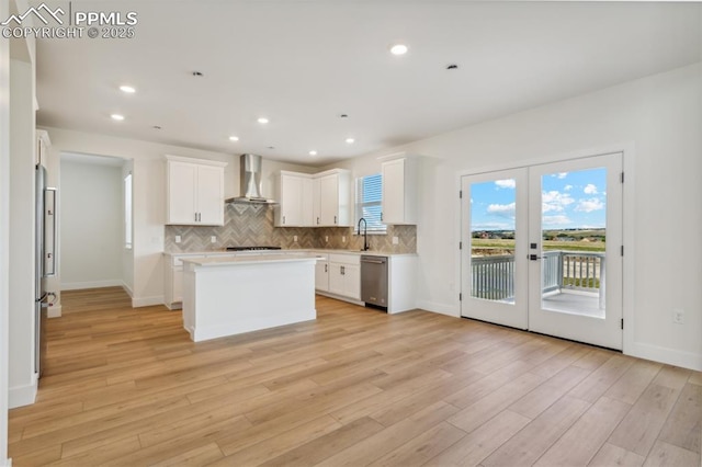 kitchen featuring white cabinets, wall chimney exhaust hood, a kitchen island, and appliances with stainless steel finishes