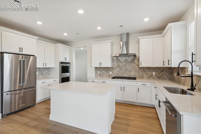 kitchen featuring white cabinetry, sink, wall chimney range hood, a kitchen island, and appliances with stainless steel finishes