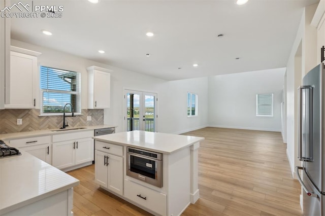 kitchen featuring a center island, sink, stainless steel appliances, decorative backsplash, and white cabinets