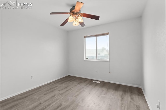 spare room with a ceiling fan, visible vents, baseboards, and wood finished floors