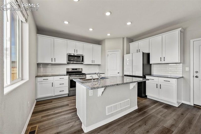 kitchen with a center island with sink, white cabinets, light stone counters, and stainless steel appliances