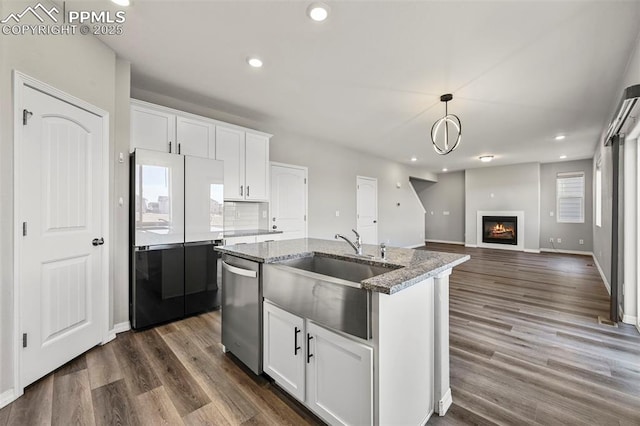 kitchen with white cabinets, a center island with sink, stainless steel dishwasher, and light stone counters