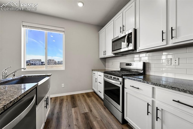 kitchen with white cabinets, dark hardwood / wood-style floors, dark stone countertops, and appliances with stainless steel finishes