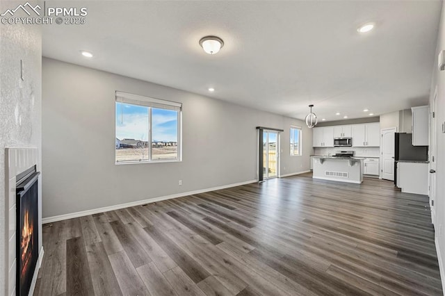 unfurnished living room with a healthy amount of sunlight, dark hardwood / wood-style flooring, and an inviting chandelier