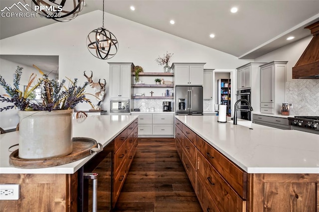 kitchen featuring decorative backsplash, appliances with stainless steel finishes, a large island with sink, pendant lighting, and an inviting chandelier