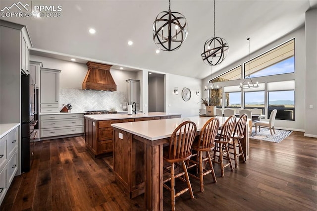 kitchen with a kitchen island with sink, vaulted ceiling, decorative backsplash, decorative light fixtures, and custom range hood