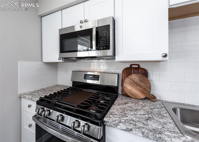 kitchen featuring decorative backsplash, white cabinetry, light stone counters, and appliances with stainless steel finishes