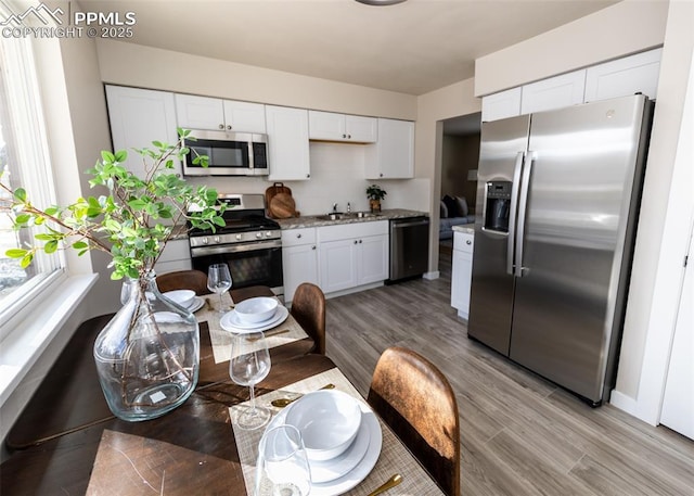 kitchen featuring light stone countertops, appliances with stainless steel finishes, sink, white cabinets, and light hardwood / wood-style floors