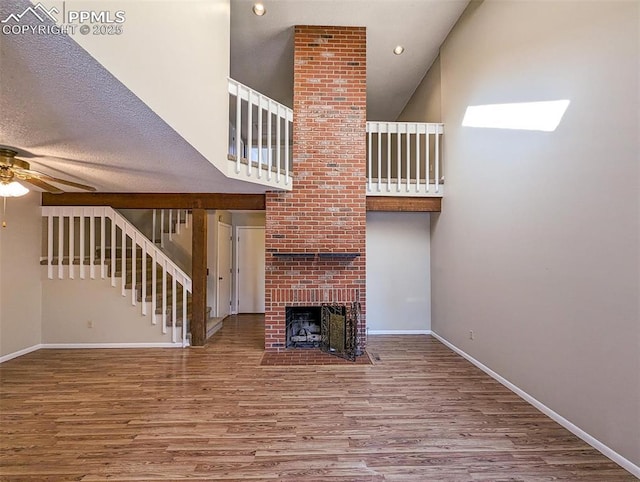 unfurnished living room featuring hardwood / wood-style floors, a textured ceiling, a brick fireplace, and ceiling fan