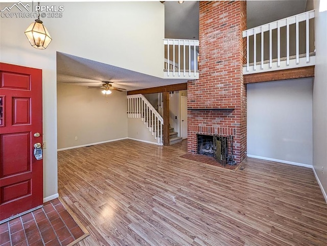 unfurnished living room with a fireplace, a towering ceiling, dark hardwood / wood-style floors, and ceiling fan