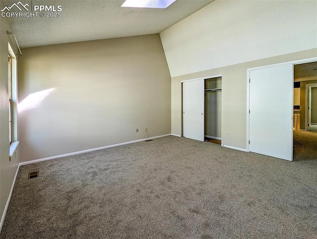 unfurnished bedroom with carpet flooring, vaulted ceiling with skylight, and a textured ceiling