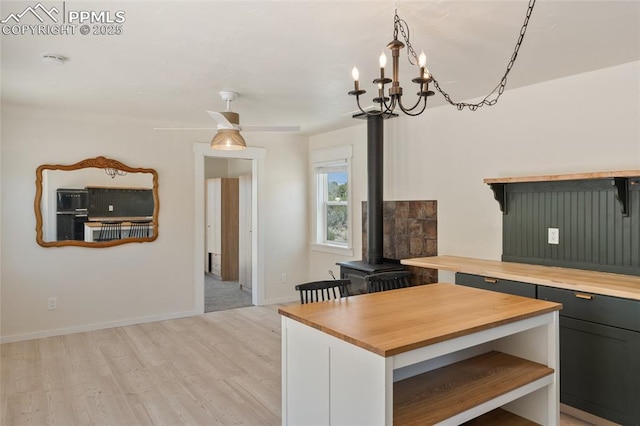 kitchen with a wood stove, ceiling fan with notable chandelier, light hardwood / wood-style flooring, decorative light fixtures, and butcher block counters