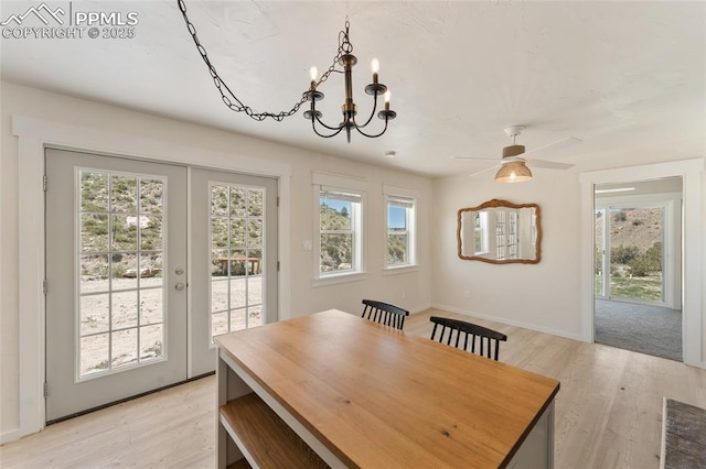 dining room with ceiling fan with notable chandelier, french doors, a wealth of natural light, and light hardwood / wood-style flooring