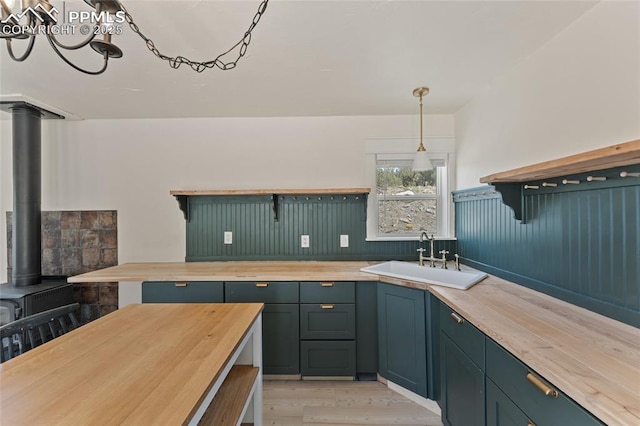 kitchen with a wood stove, sink, hanging light fixtures, light hardwood / wood-style floors, and butcher block counters