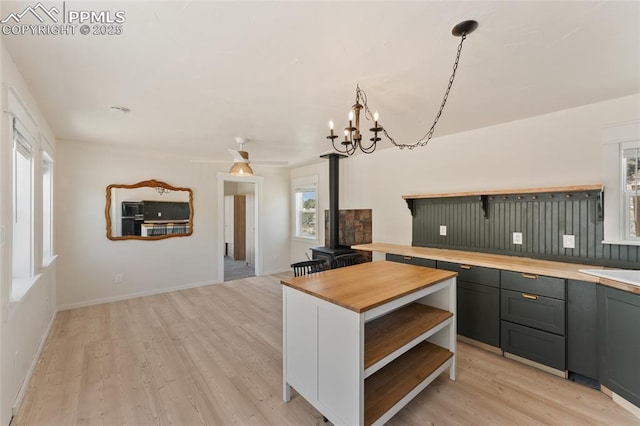 kitchen with a wood stove, light hardwood / wood-style flooring, pendant lighting, and butcher block counters