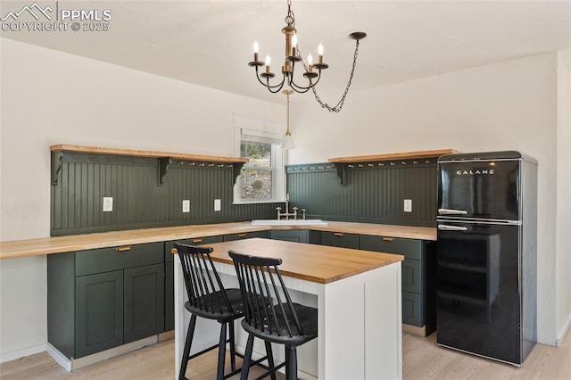 kitchen featuring a center island, black fridge, sink, decorative light fixtures, and a notable chandelier