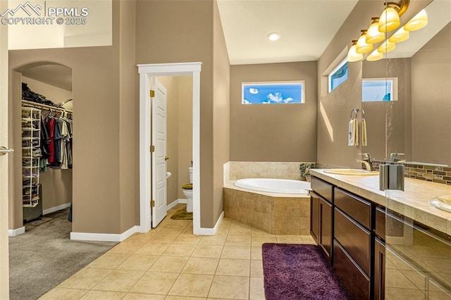 bathroom with tile patterned flooring, vanity, a relaxing tiled tub, and toilet