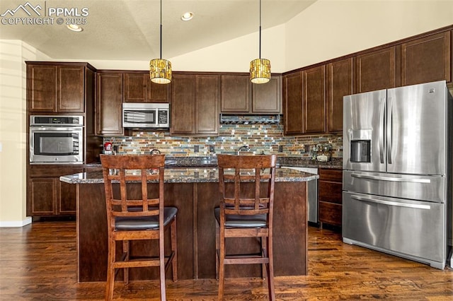 kitchen with hanging light fixtures, a kitchen island, dark stone counters, and appliances with stainless steel finishes