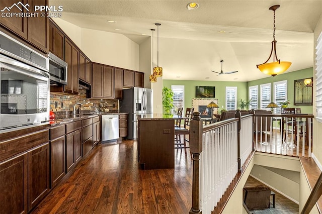 kitchen with appliances with stainless steel finishes, a center island, dark brown cabinetry, decorative light fixtures, and vaulted ceiling