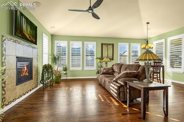 living room featuring a tiled fireplace, vaulted ceiling, ceiling fan with notable chandelier, and dark hardwood / wood-style flooring