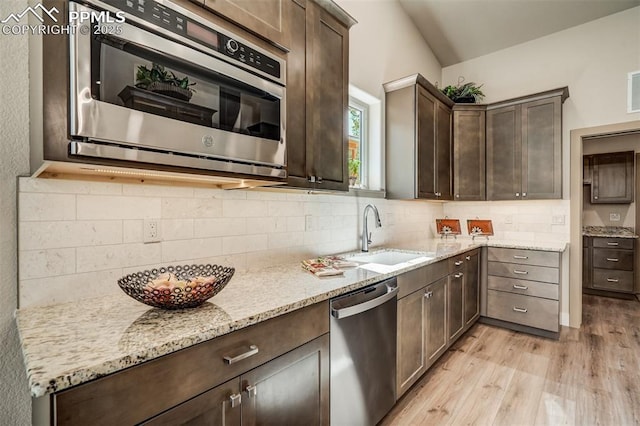 kitchen featuring light stone counters, stainless steel dishwasher, dark brown cabinetry, sink, and light hardwood / wood-style flooring