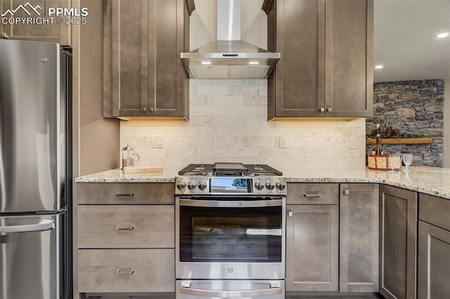 kitchen with light stone counters, wall chimney range hood, backsplash, and appliances with stainless steel finishes