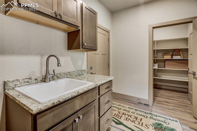 kitchen with dark brown cabinets, light wood-type flooring, light stone counters, and sink