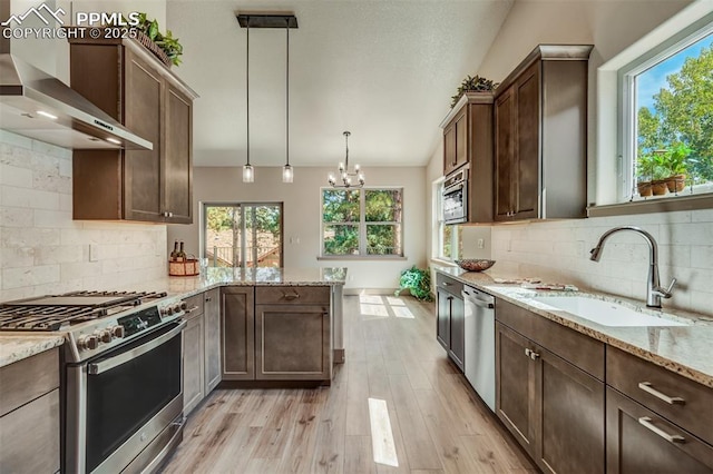 kitchen featuring backsplash, sink, wall chimney exhaust hood, decorative light fixtures, and stainless steel appliances