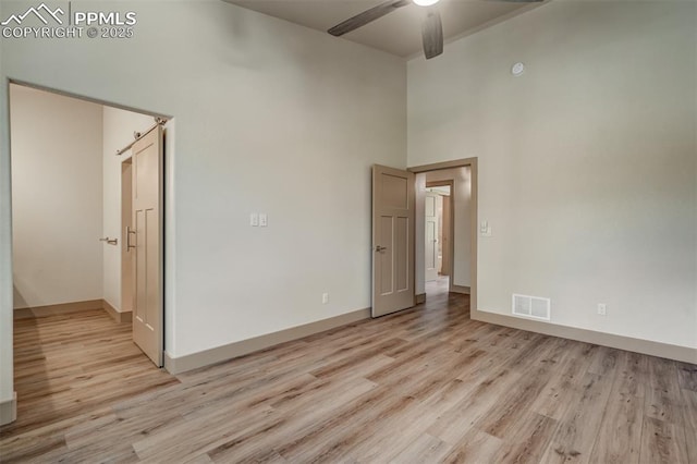 unfurnished room with ceiling fan, light hardwood / wood-style flooring, and a towering ceiling