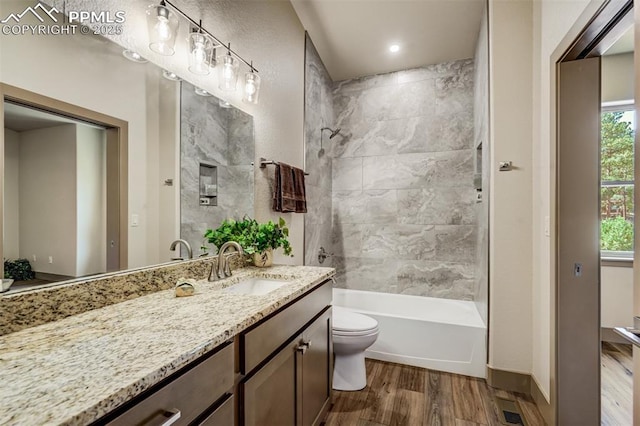 full bathroom featuring hardwood / wood-style flooring, vanity, tiled shower / bath combo, and toilet