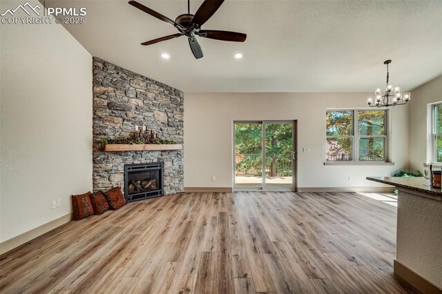 unfurnished living room with ceiling fan with notable chandelier, light hardwood / wood-style floors, and a stone fireplace