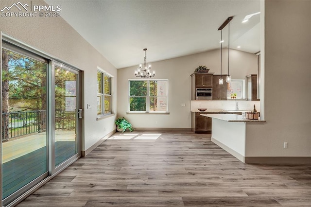 kitchen featuring a notable chandelier, kitchen peninsula, lofted ceiling, decorative light fixtures, and light wood-type flooring