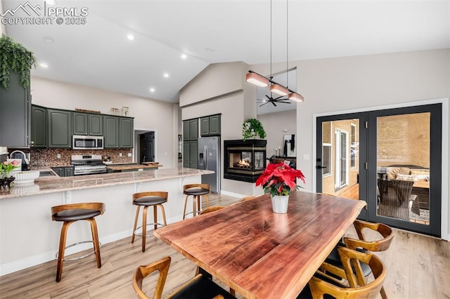 dining space featuring vaulted ceiling, a multi sided fireplace, sink, and light hardwood / wood-style flooring