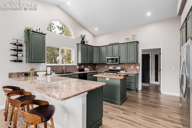 kitchen featuring kitchen peninsula, appliances with stainless steel finishes, light stone countertops, high vaulted ceiling, and green cabinetry